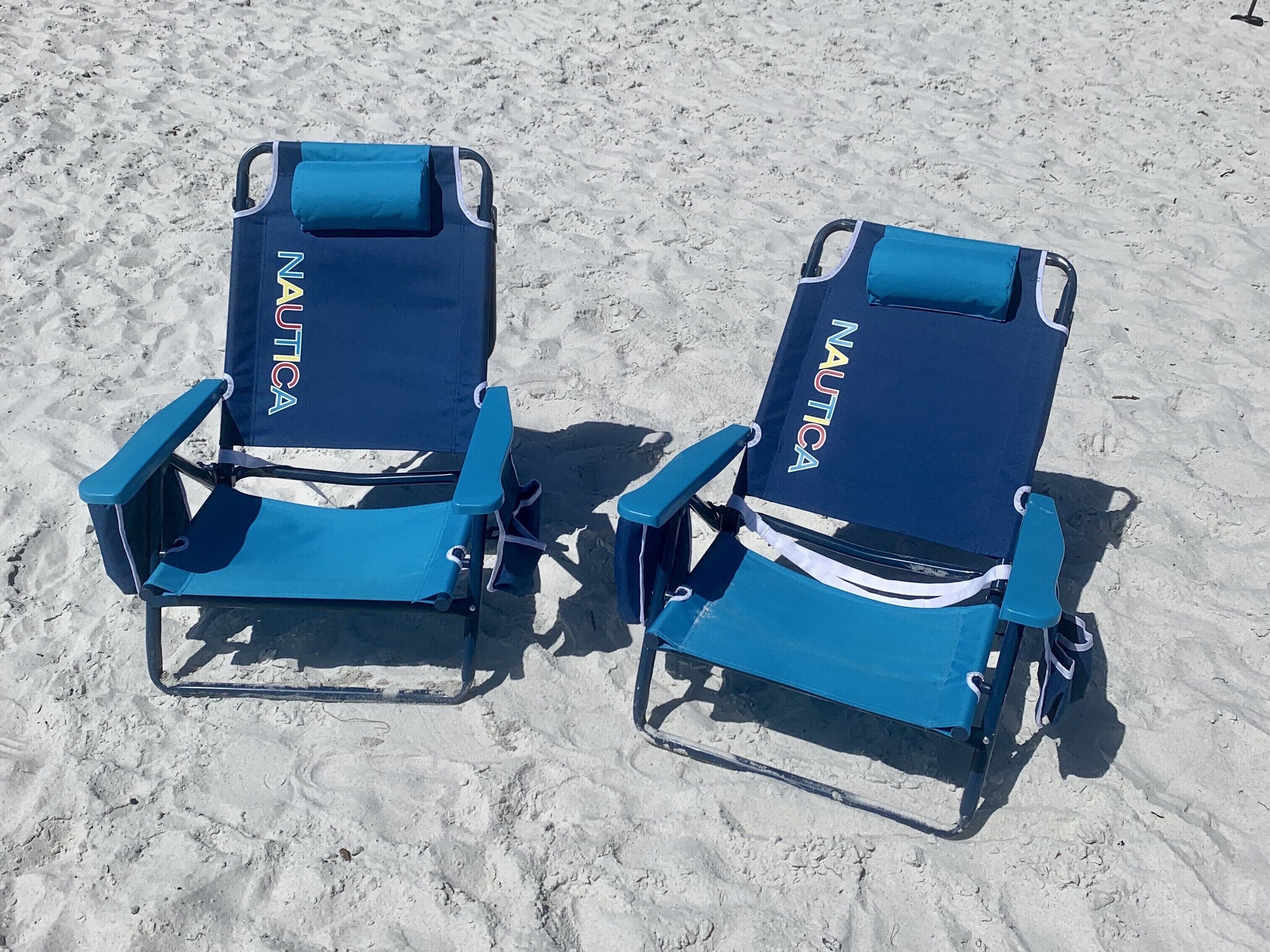 Two blue beach chairs with 'NAUTICA' branding on the backrests, positioned on a sandy beach.