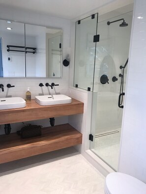 A modern bathroom with two white sinks, a mirror, and a glass-enclosed shower.