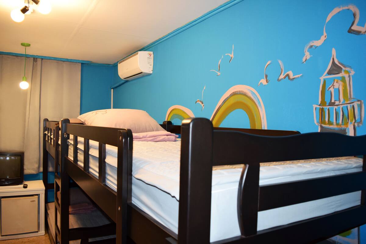 A bunk bed with a TV, a small desk, and a wall mural with birds and a rainbow.