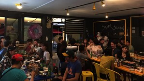 Ein belebtes Restaurant mit mehreren Tischen und Stühlen, einem Deckenventilator und einem Schild an der Wand.