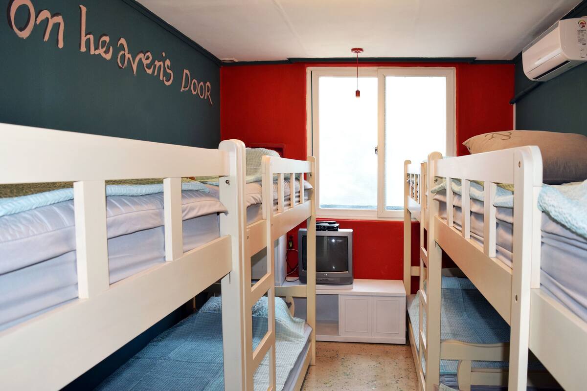 A bunk bed room with a television on the lower bunk, a window with a view, and a door with a sign.