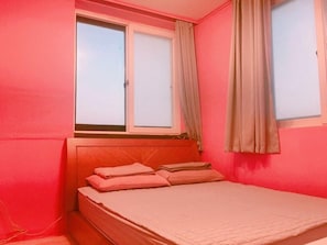 Ein kleines Schlafzimmer mit einem Einzelbett, einem Fenster mit Vorhängen und einer schlichten Wand.