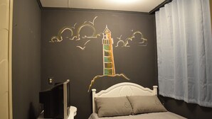 Ein Schlafzimmer mit Bett, einem Fernseher auf einem Schrank und Wandgemälde eines Leuchtturms.