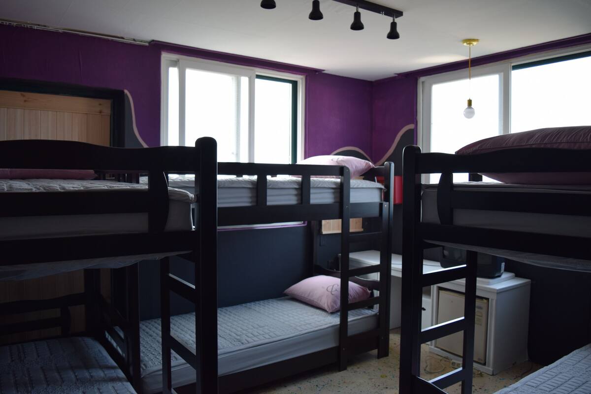 A dormitory room with bunk beds, a small desk, and a window providing natural light.