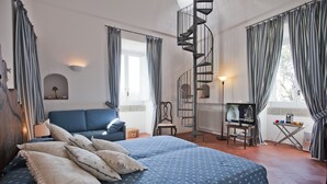 Un dormitorio con una cama grande, una escalera en espiral, un televisor y una mesita con tazas de colores.