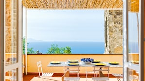 Un espacio de comedor al aire libre con una mesa preparada para cuatro personas, con vista panorámica al mar y a las montañas.