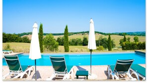 Zona de piscina amb gandules i ombrel·les, amb vista a un paisatge idíl·lic ple d'arbres i turons.