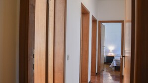 Un pasillo con puertas de madera que dan a un dormitorio con cama y mesita de noche.