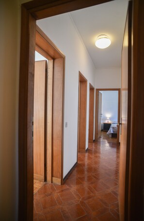 A hallway with wooden doors leading to a bedroom with a bed and a nightstand.