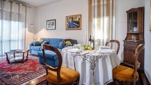 Un comedor con una mesa dispuesta para cuatro personas, un sofá azul, un armario de madera y una alfombra roja estampada.