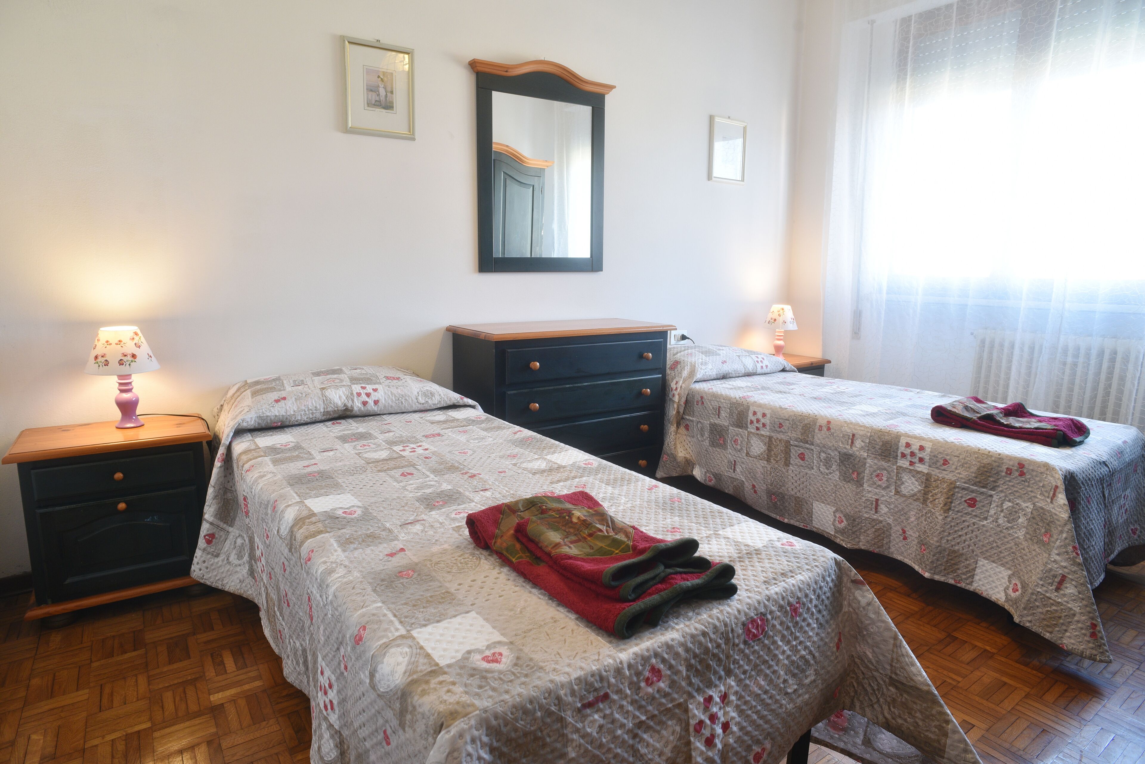Un dormitorio con dos camas, un aparador, un espejo y una ventana con cortinas.