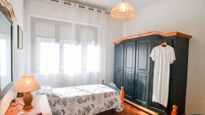 Un dormitorio con cama, mesita de noche con lámpara, armario y ropa colgada.
