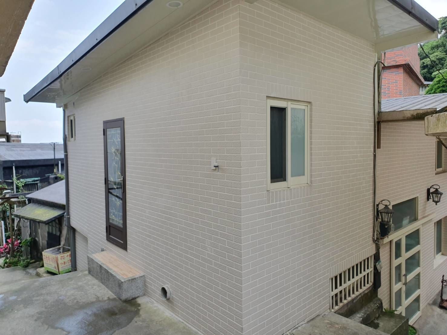 Un edificio de dos pisos con fachada de ladrillo claro, una ventana pequeña y una puerta.
