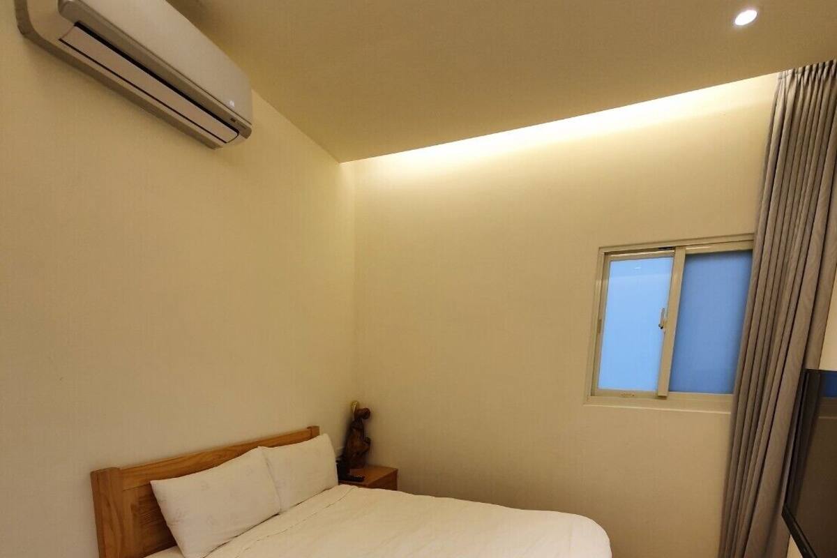 Quarto com cama de madeira, roupa de cama branca, ar condicionado, janela com cortinas e televisão na parede.