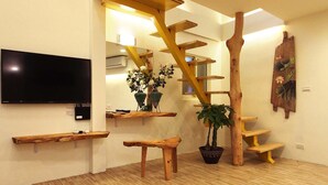 A modern living room with a wooden staircase, a flat-screen TV, wooden benches, and potted plants. - Chien Ching B&B (New Taipei City)