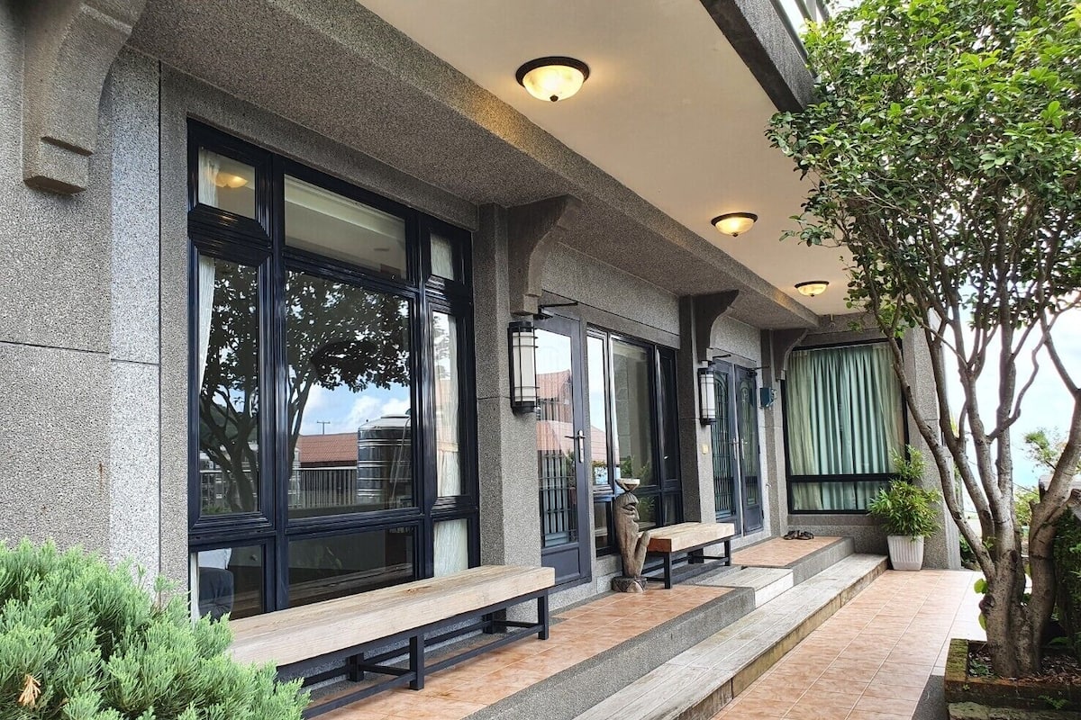 Fachada de edifício com janelas amplas, um banco e uma árvore.