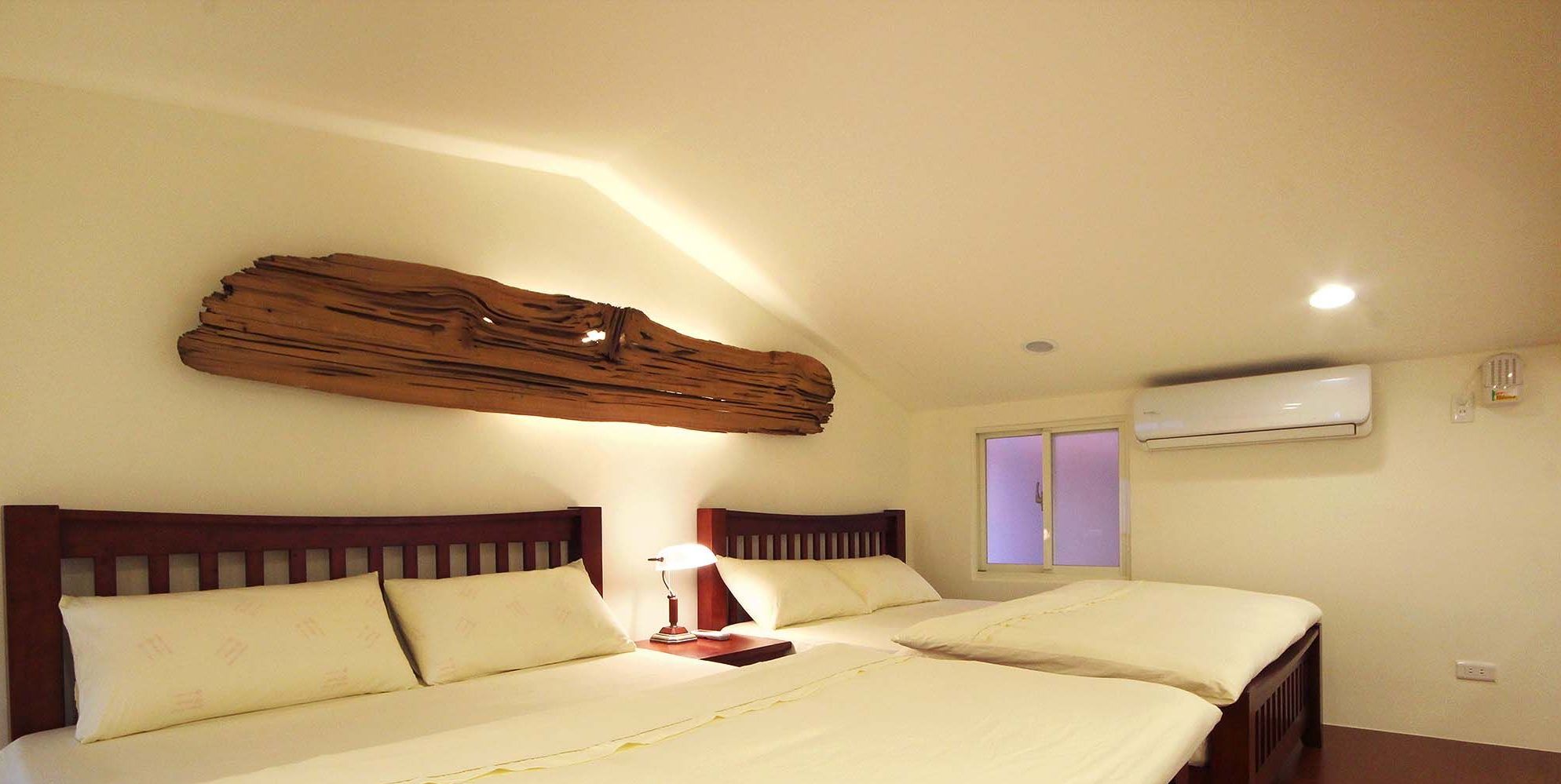 A bedroom with two beds, a wooden headboard, a bedside lamp, and an air conditioning unit.