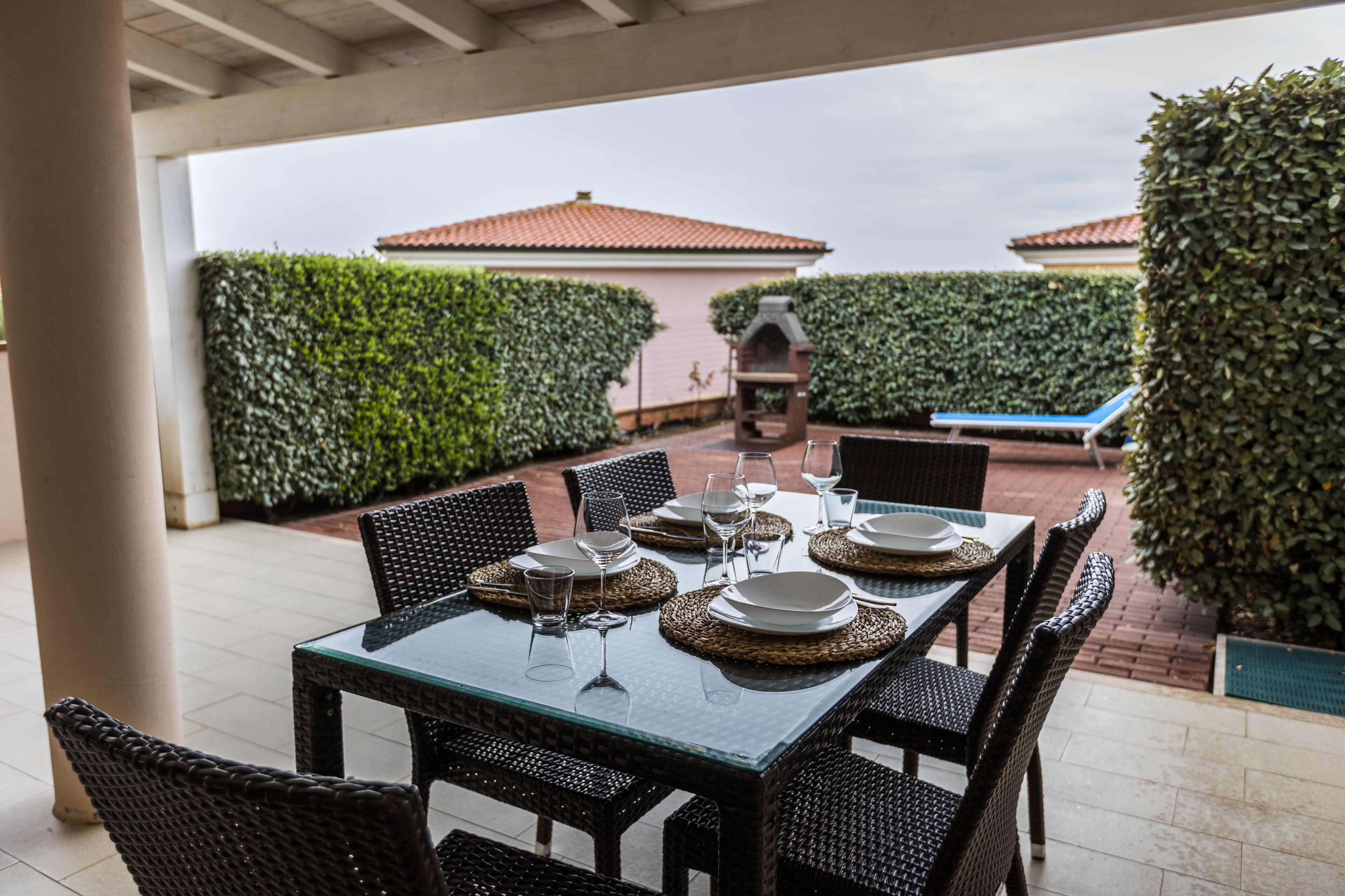 A covered outdoor dining area with a table set for six, surrounded by wicker chairs.