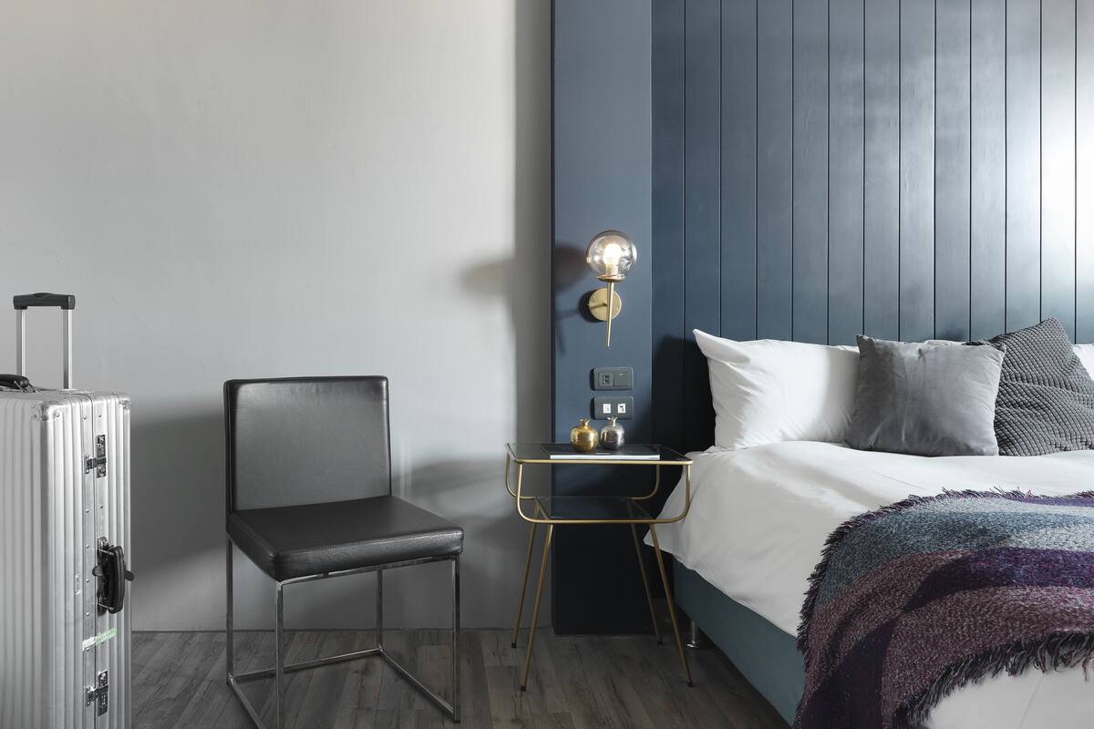 Una habitación de hotel con cama, una silla, un escritorio y una maleta.