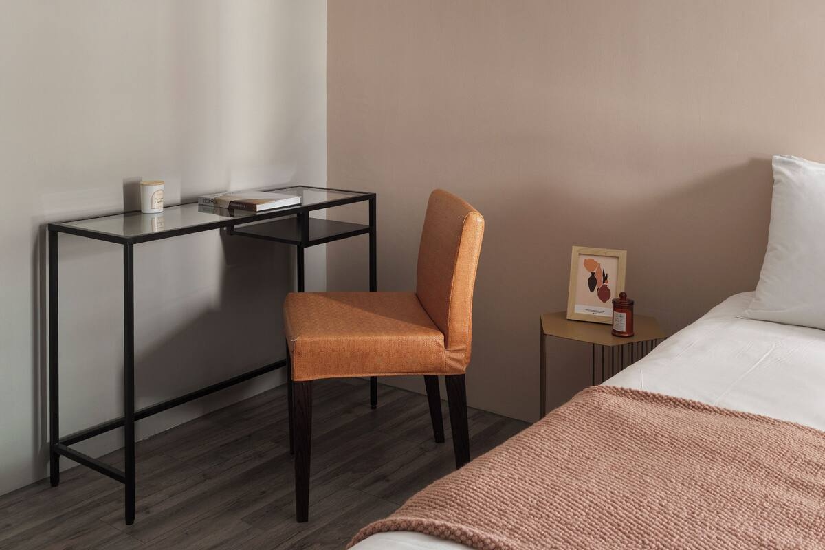Habitación de hotel con cama, escritorio, silla y una pequeña mesa con un marco de fotos y una vela.