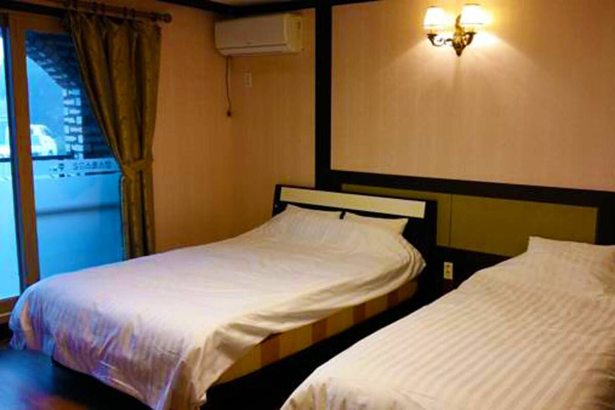 Hotelkamer met twee enkele bedden, een raam met gordijnen, een airconditioning en een wandlamp.