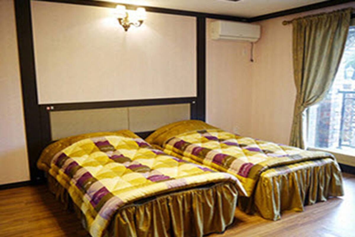 Een kamer met twee bedden, een raam met gordijnen en een luchtverkoeler aan de muur.