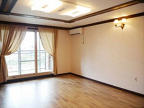Ein Zimmer mit Holzboden, einem großen Fenster mit Vorhängen und einer Wandleuchte.