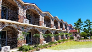 Fila de edificios de ladrillo con ventanas y balcones de arco, unidades de aire acondicionado y un jardín bien cuidado.