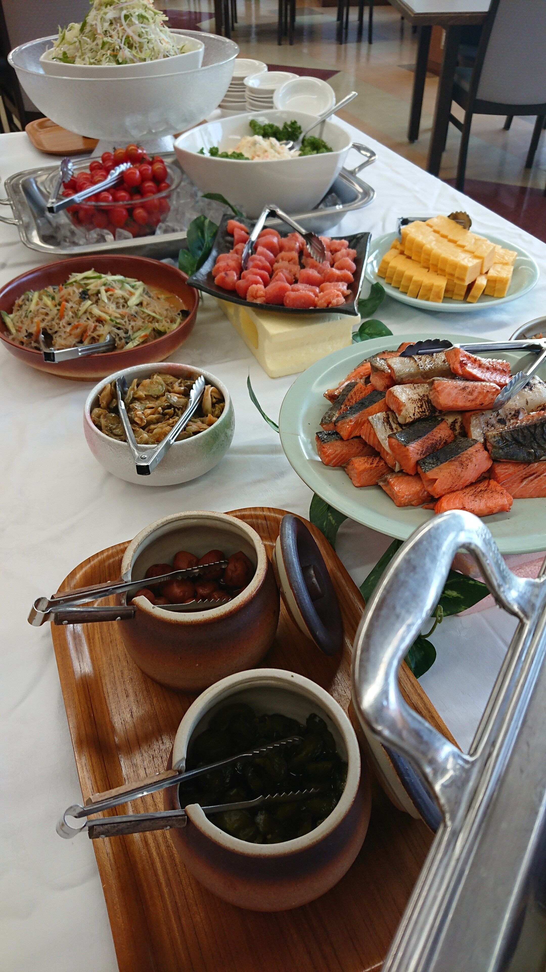 A buffet table with various dishes including salads, grilled salmon, and cheese.