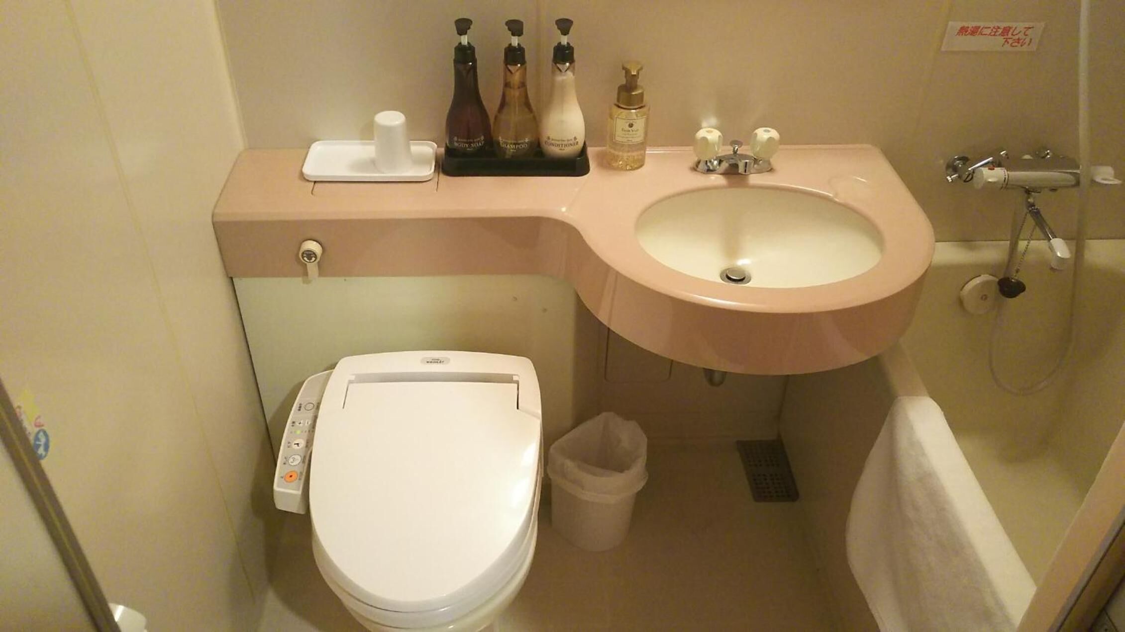 Un baño pequeño con inodoro, lavamanos y ducha. Hay artículos de aseo en la encimera.