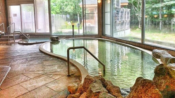 An indoor swimming pool with clear glass walls, a tiled floor, and a wooden ceiling.