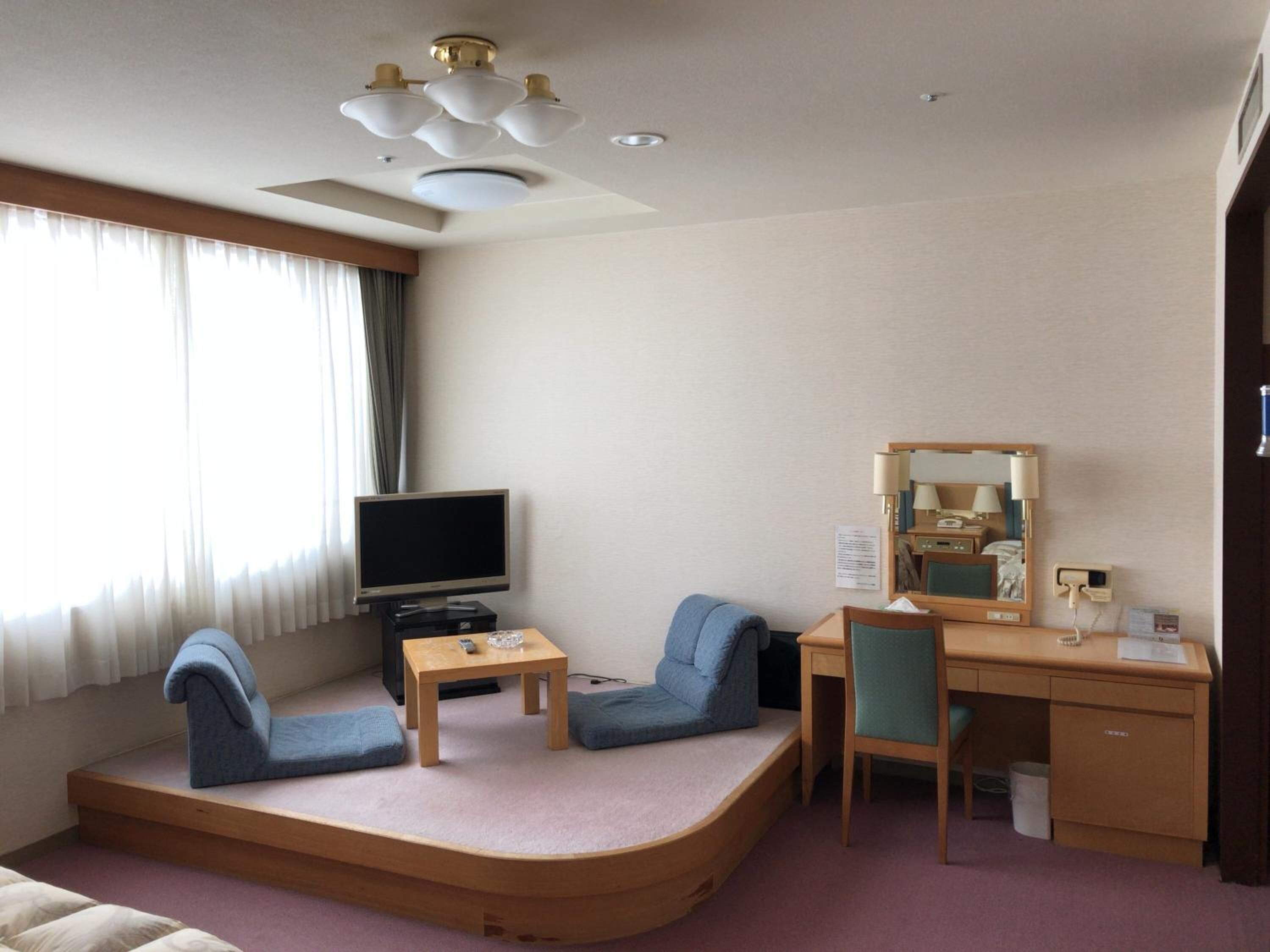Ein Hotelzimmer mit einer gebogenen Couch, einem Schreibtisch, einem Fernseher und einem Spiegel.