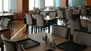 A spacious conference room with multiple tables and chairs, large windows, and a decorative ceiling.