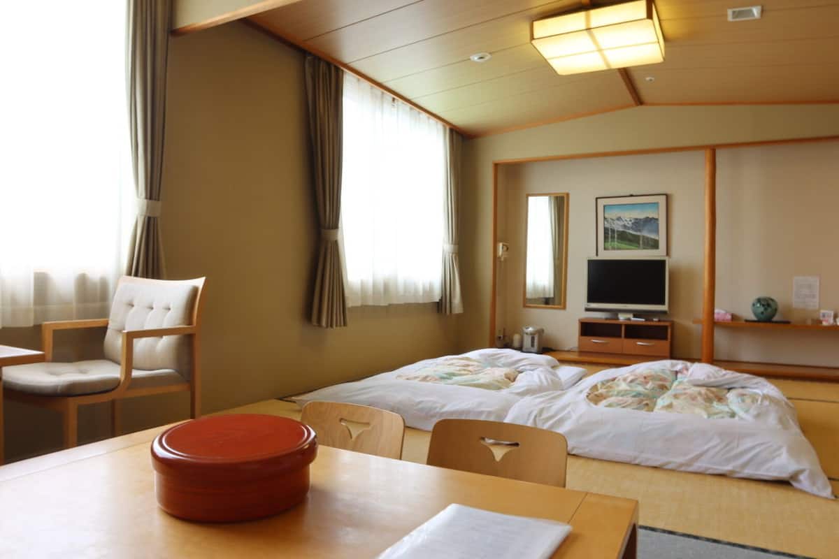 Ein Hotelzimmer mit zwei Betten, einem Fernseher, einem Tisch mit einem roten Topf und einem Stuhl.