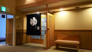 A hotel lobby with a wooden bench, a sliding door with a black banner, and a reception area with a lighted exit sign.