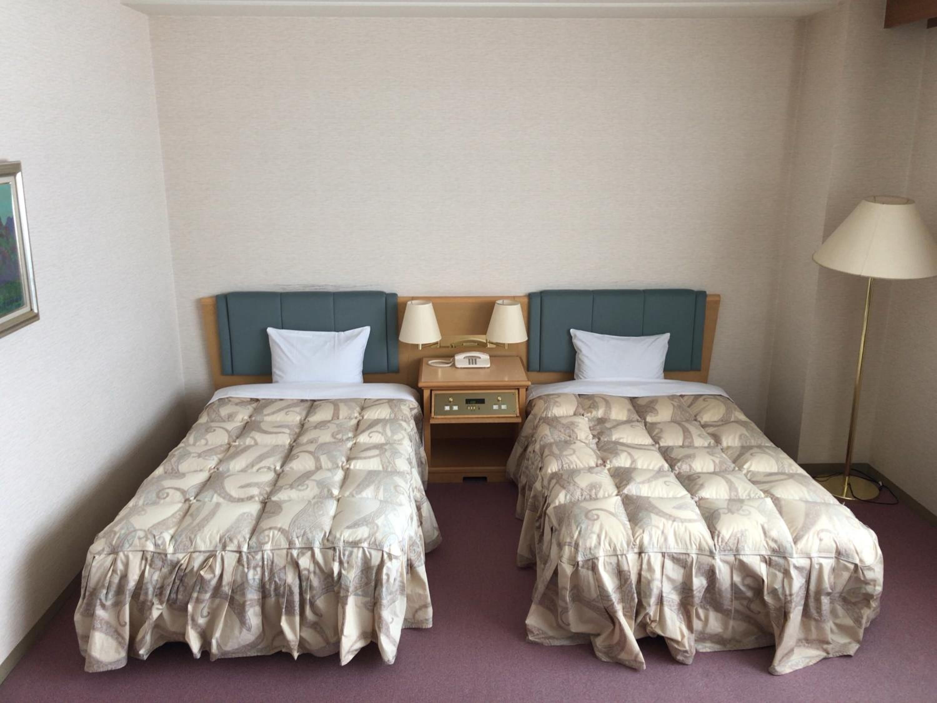 Quarto de hotel com duas camas de solteiro, cada uma com cabeceira, mesas de cabeceira, abajures e painel de controle.