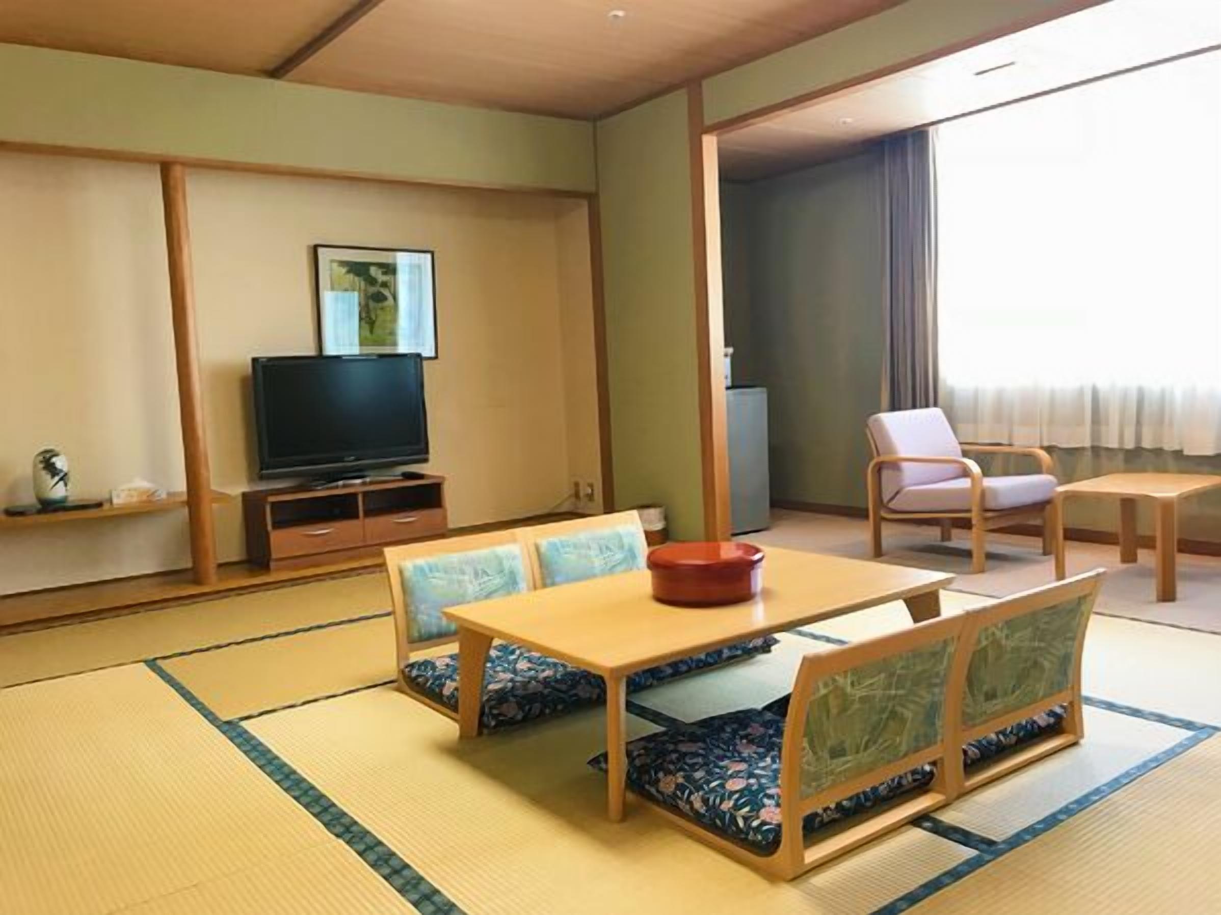 A traditional Japanese-style room with tatami flooring, a television, a dining table with cushions, and a sofa.