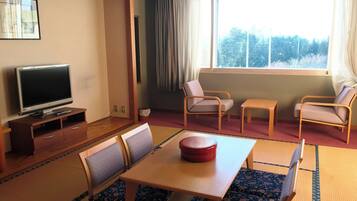 Una habitación con una televisión sobre un soporte de madera, una mesa de comedor con sillas y una ventana con cortinas.