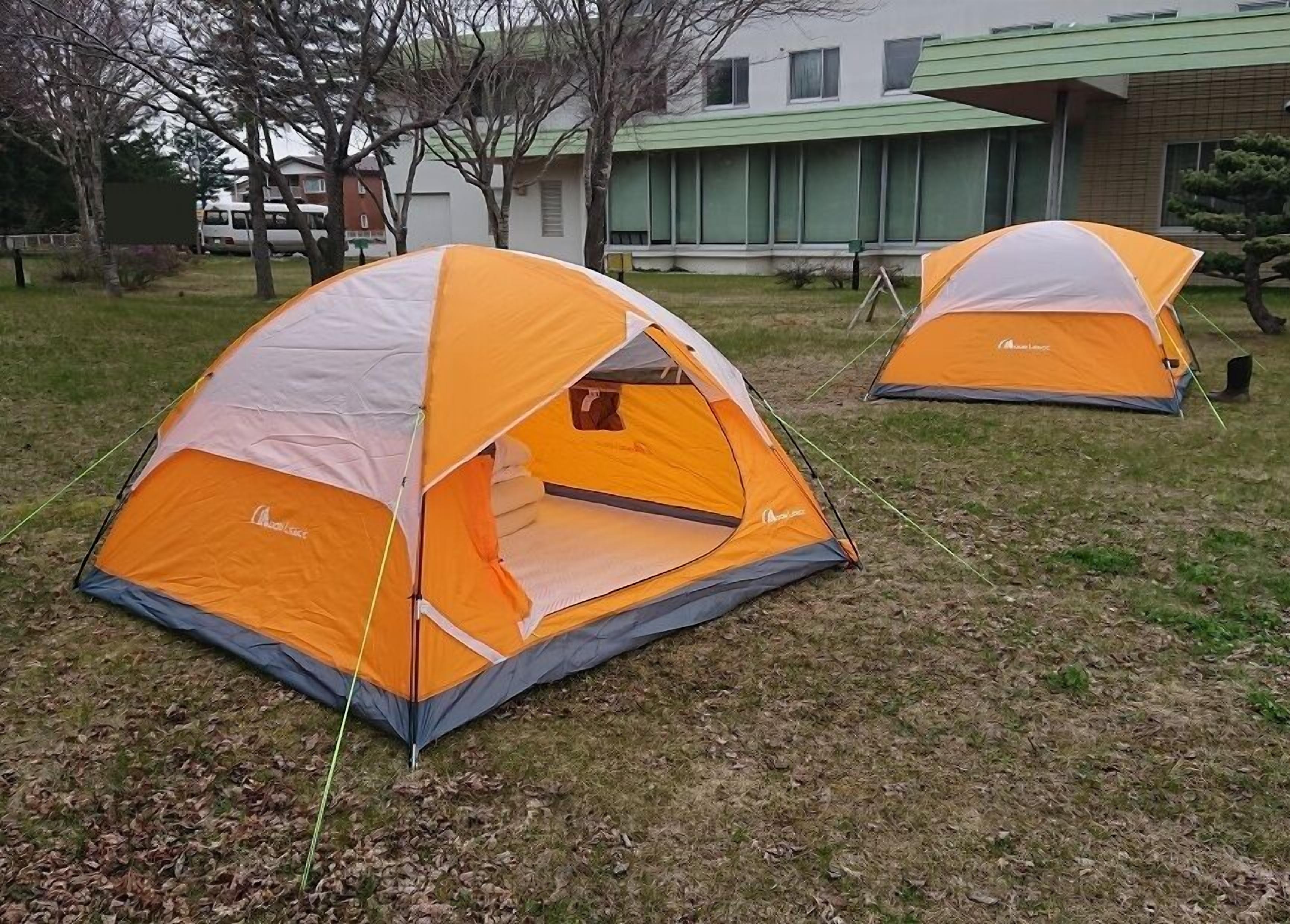 Twee kampeertenten met een koepelvorm, oranje en grijze kleuren, en een zichtbaar merknaam op de zijkant.