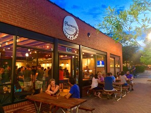 An outdoor seating area of a restaurant with a sign indicating it offers a pharmacy, bottle, and beverage service.