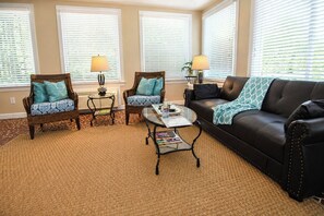 A living room with a black leather sofa, two wicker armchairs, a glass coffee table, and two lamps. - The Cary House in Downtown Cary (Cary)