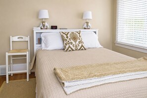 A neatly arranged bedroom with a bed, two bedside lamps, a nightstand, a chair, and a window with blinds.