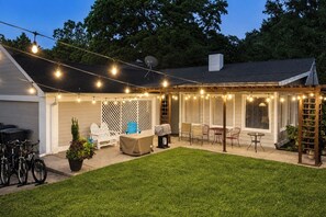 A backyard with a covered patio, outdoor seating, and string lights.