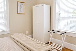 A room with a bed, a wardrobe, a window with blinds, and a drying rack.