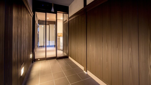 A hallway with wooden paneling and a tiled floor leading to a room with a sliding door. - Le Studio Gojo Takakura (Kyoto)