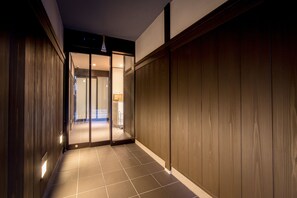 A hallway with wooden paneling and a tiled floor leading to a room with a sliding door. - Le Studio Gojo Takakura (Kyoto)