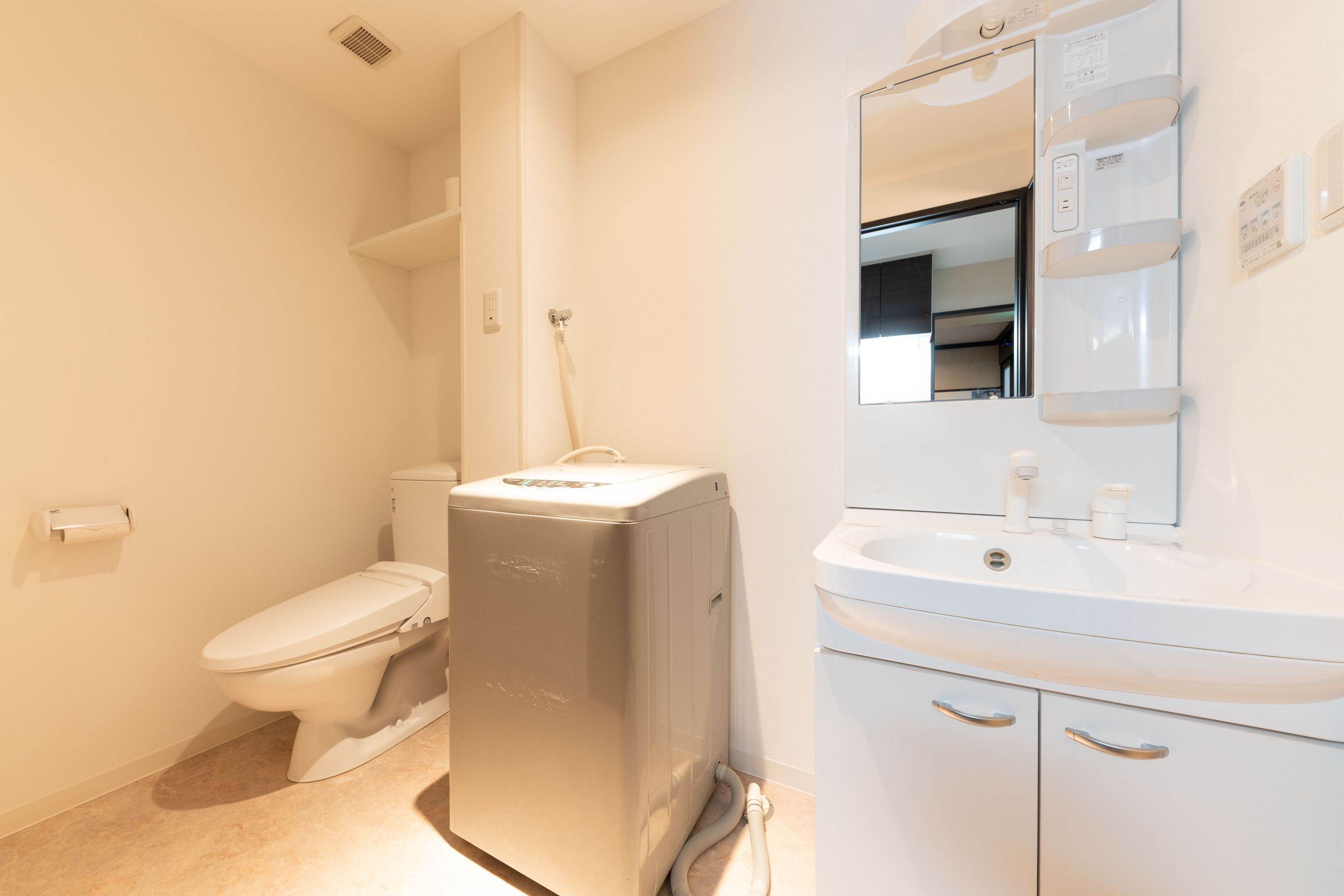 Une salle de bain comprenant des toilettes, un lave-linge compact, un lavabo et un miroir.