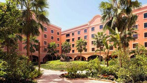 A hotel courtyard with palm trees, a central pathway, and a building with multiple windows and balconies.