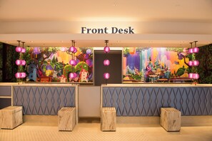 A reception area with a 'Front Desk' sign, two wooden benches, and a colorful mural with hanging pink lanterns.