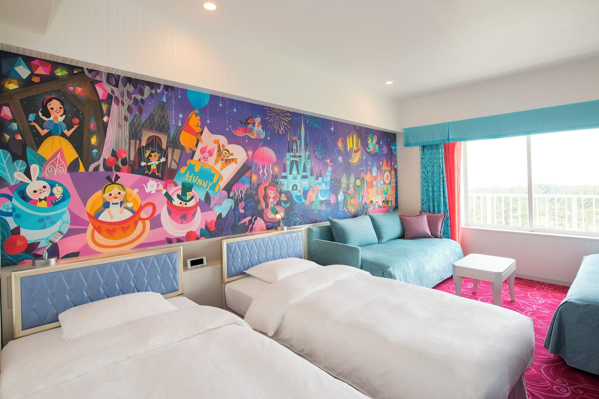 A hotel room with two beds, a colorful mural, a balcony with a view, and a window with curtains.